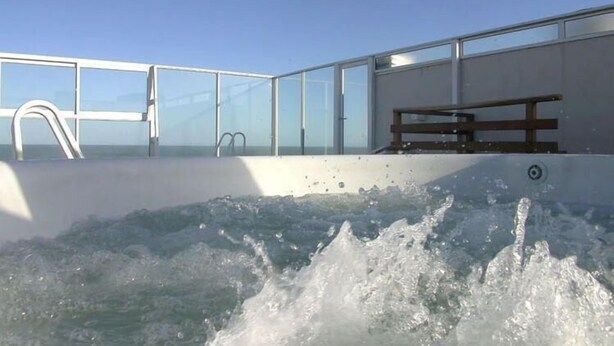 A hot tub with a wooden bench and glass railings. - Portasol Apart Hotel (Pinamar)