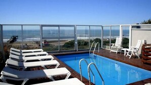 A rooftop pool with clear views of the ocean and beach, surrounded by white lounge chairs. - Portasol Apart Hotel (Pinamar)
