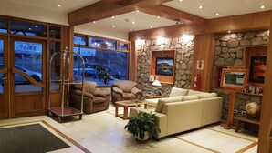 A spacious lobby with a stone wall, a large sofa, and a wooden reception desk. - Hotel Tierra del Fuego (Ushuaia)