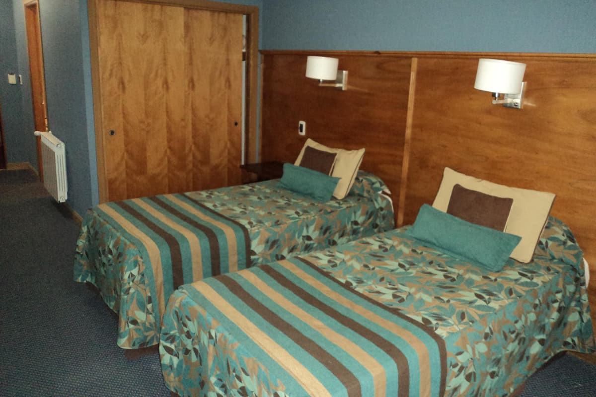 Una habitación con dos camas, un armario de madera y dos lámparas fijadas a la pared.