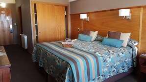 A hotel room with a large bed, a wooden headboard, two bedside lamps, a nightstand, and a basket on the bed. - Hotel Tierra del Fuego (Ushuaia)