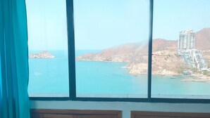 A room with a large window overlooking a coastal area with boats and a building. - Apartamento Tropical - Smr245a (Santa Marta)