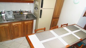 A kitchen with wooden cabinets, a stainless steel sink, a refrigerator, and a dining table with a placemat. - Apartamento Tropical - Smr245a (Santa Marta)