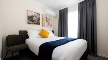 Een hotelkamer met een bed, een stoel, twee schilderijen aan de muur en een raam met gordijnen.