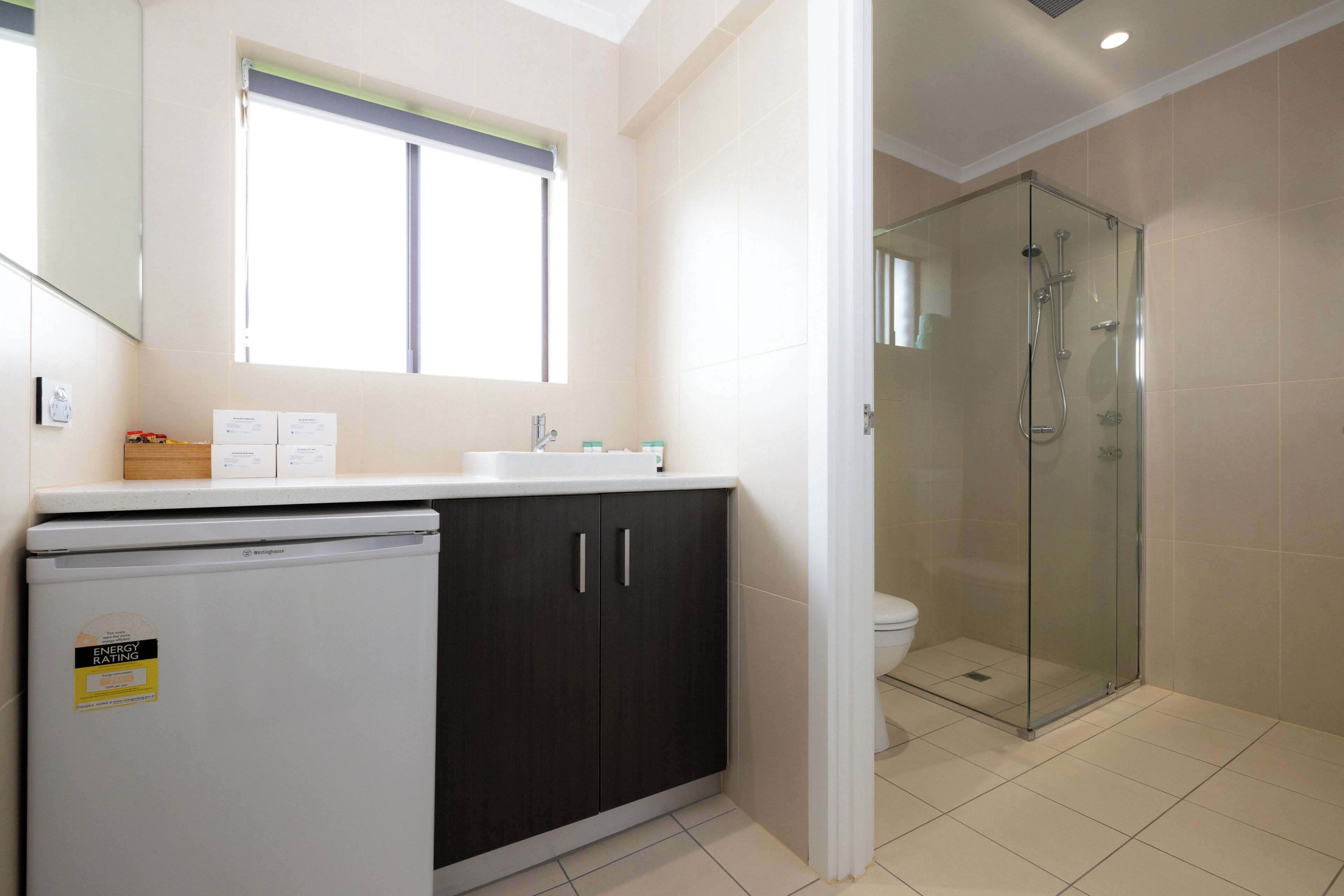 Un baño con cabina de ducha de vidrio, inodoro y refrigerador blancos.