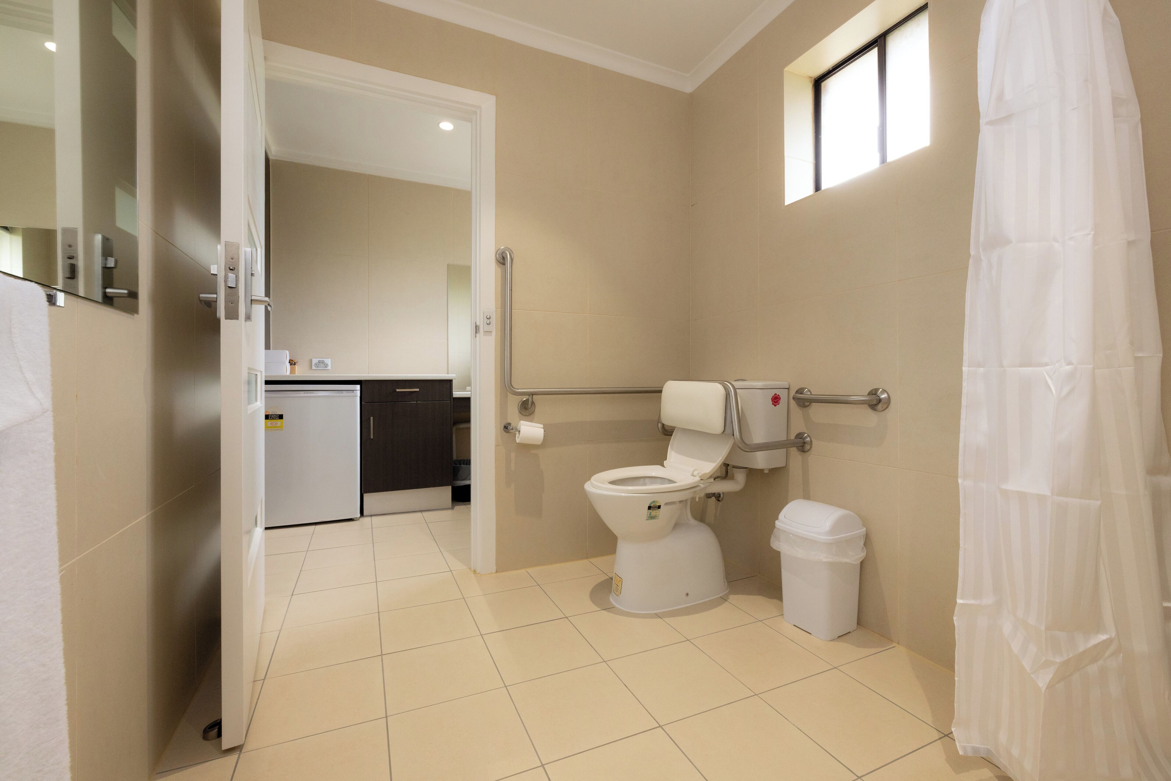 Un baño moderno con inodoro, bidé y secamanos. Cuenta con un ventanal pequeño y cortina de ducha.