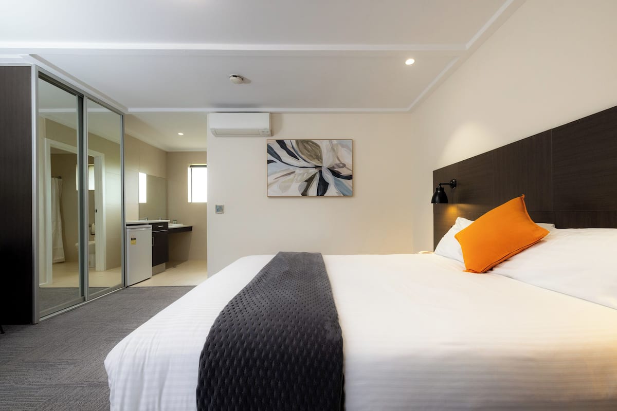 A hotel room with a bed, a nightstand, a wall-mounted lamp, and a sliding door leading to a bathroom.