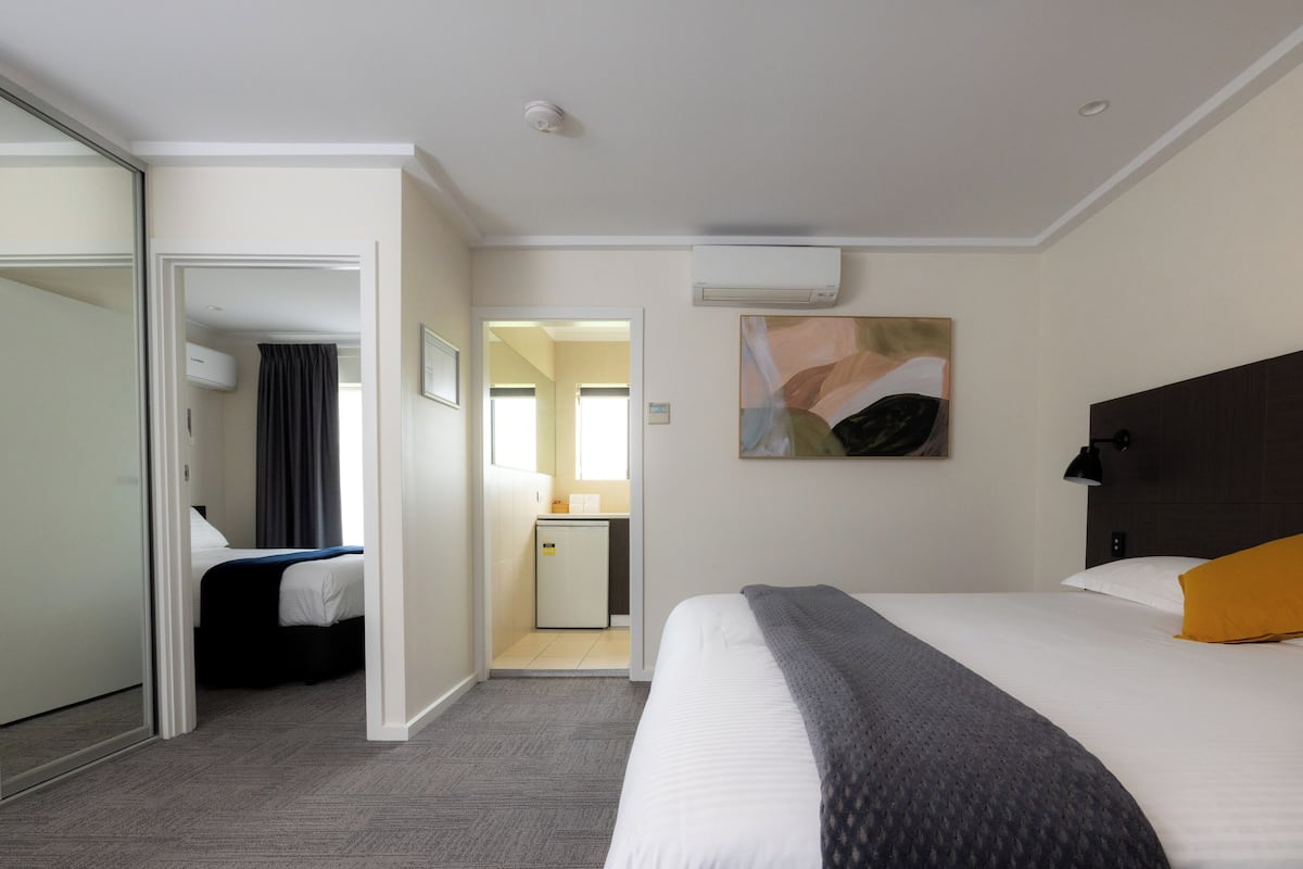 A hotel room with a bed, a desk, a mirror, and an air conditioning unit.