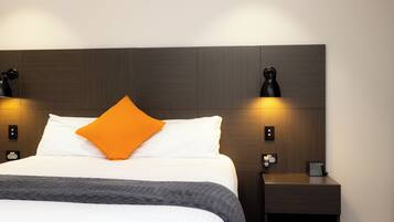 Una cama bien hecha con sábanas blancas y un almohadón naranja, flanqueada por dos apliques negros en la pared.