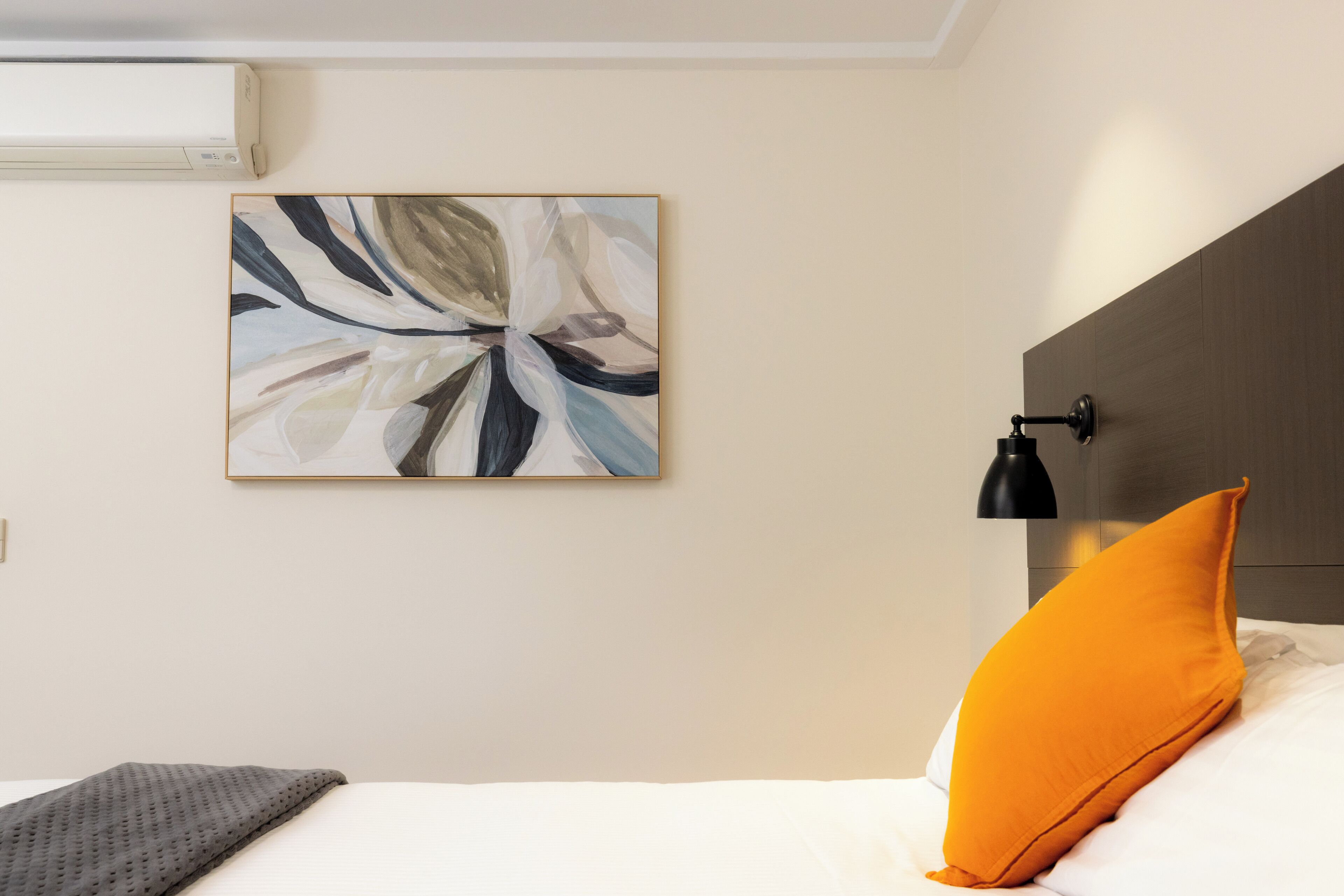 A bedroom with a bed, a pillow, a wall-mounted lamp, and an abstract painting.