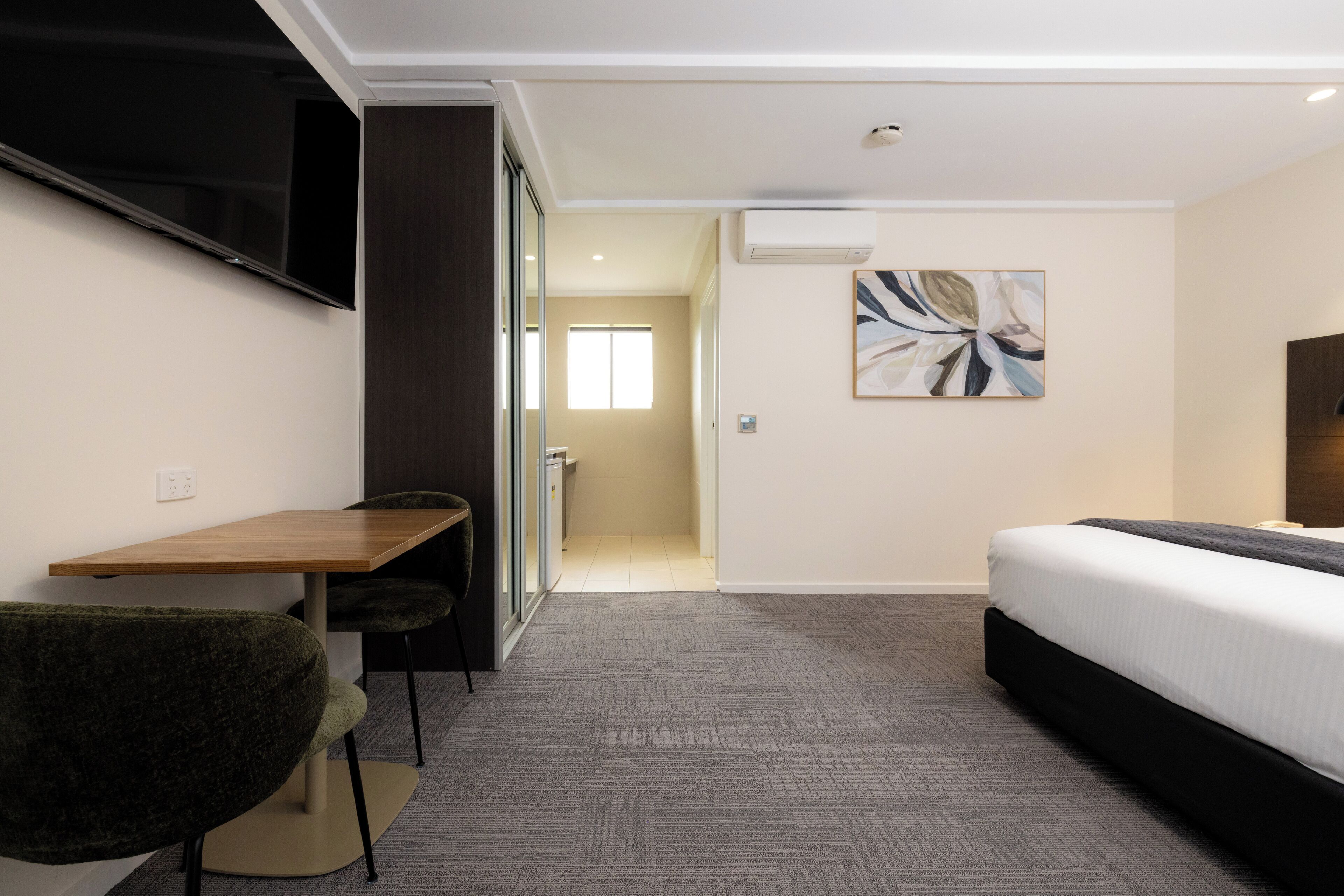 Habitación de hotel con cama, escritorio con silla, televisión montada en la pared y un cuadro en la pared.