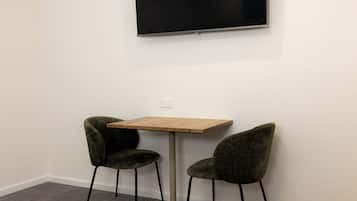 A small room with a wooden table and two green chairs, a flat-screen TV mounted on the wall, and a carpeted floor.