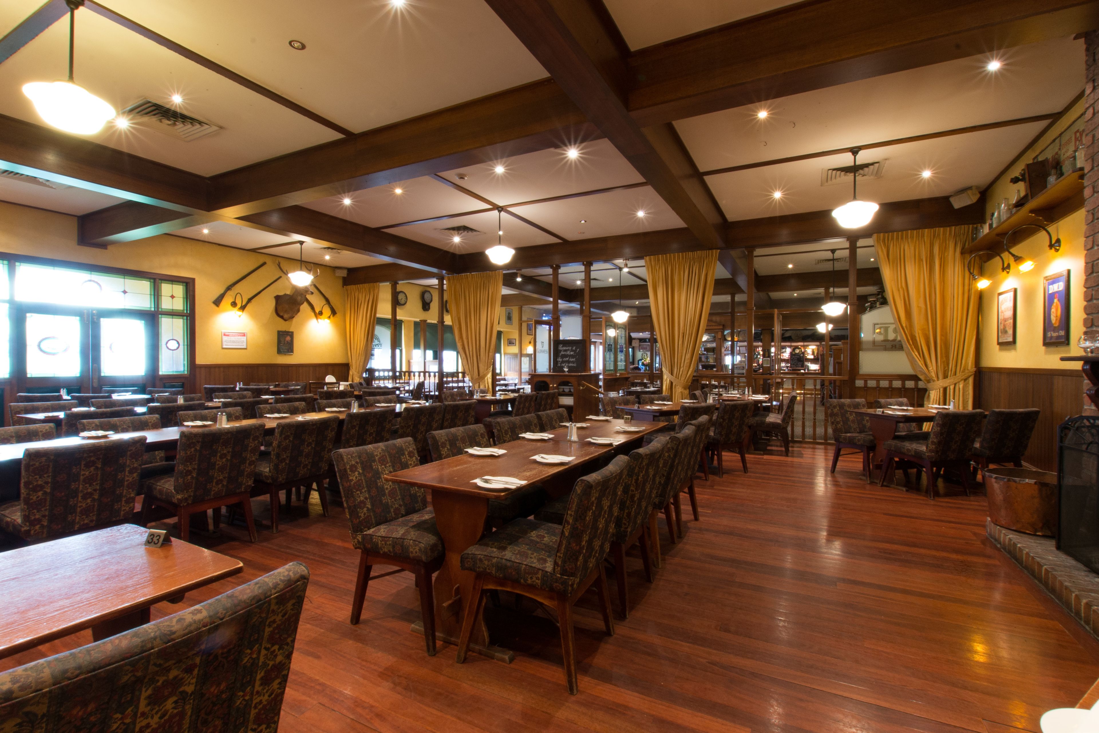 A spacious dining area with multiple tables and chairs, wooden floors, and a high ceiling with exposed beams.