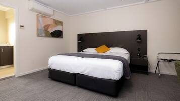 A modern hotel room with a large bed, a bedside table, a wall-mounted air conditioner, and a painting on the wall.