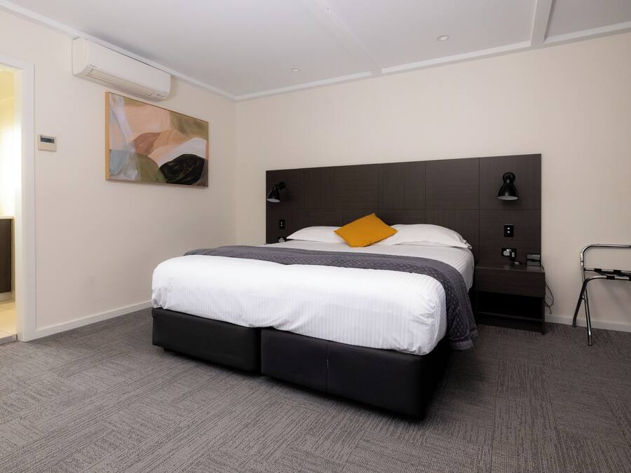 Une chambre d’hôtel moderne avec un grand lit, une table de chevet, un climatiseur fixé au mur et un tableau accroché au mur.