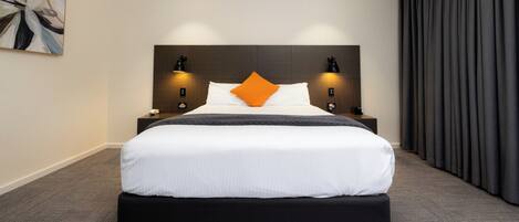 Una habitación de hotel moderna con una cama grande, dos mesitas de noche y un cabecero con iluminación integrada.