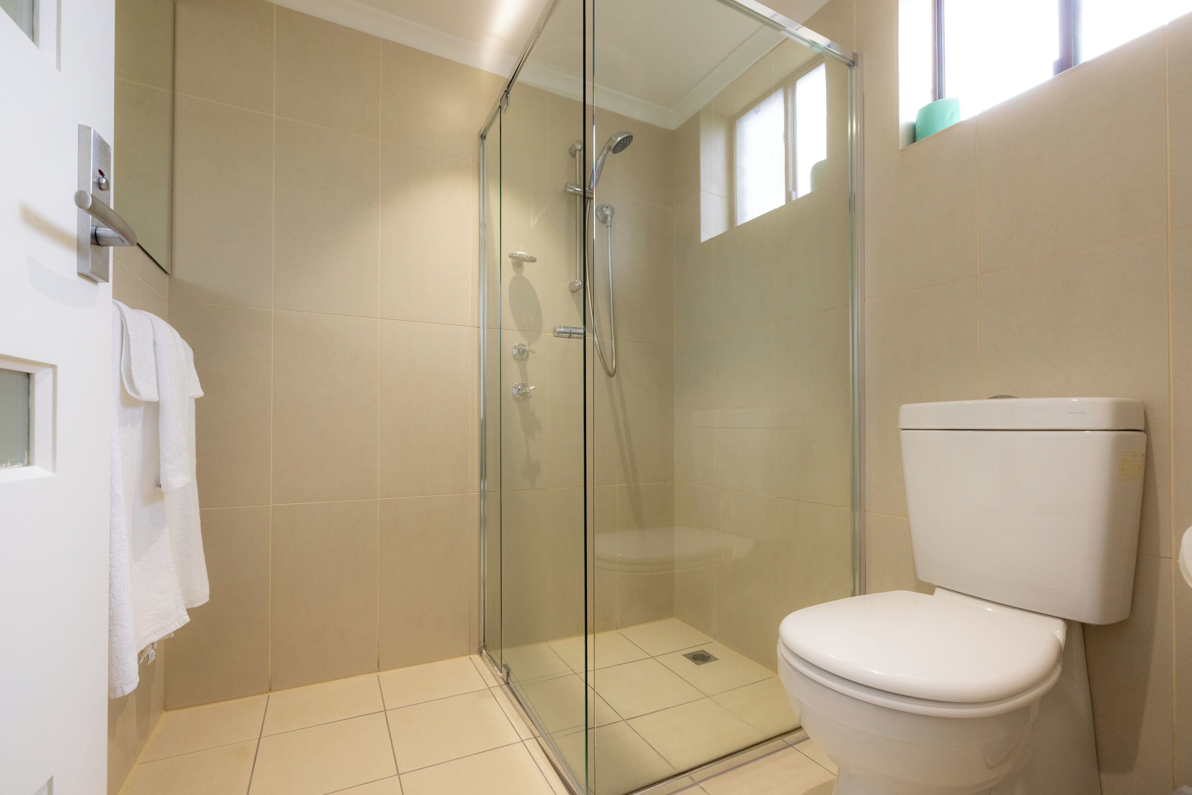 A modern bathroom with a glass-enclosed shower, a white toilet, and beige tiles.