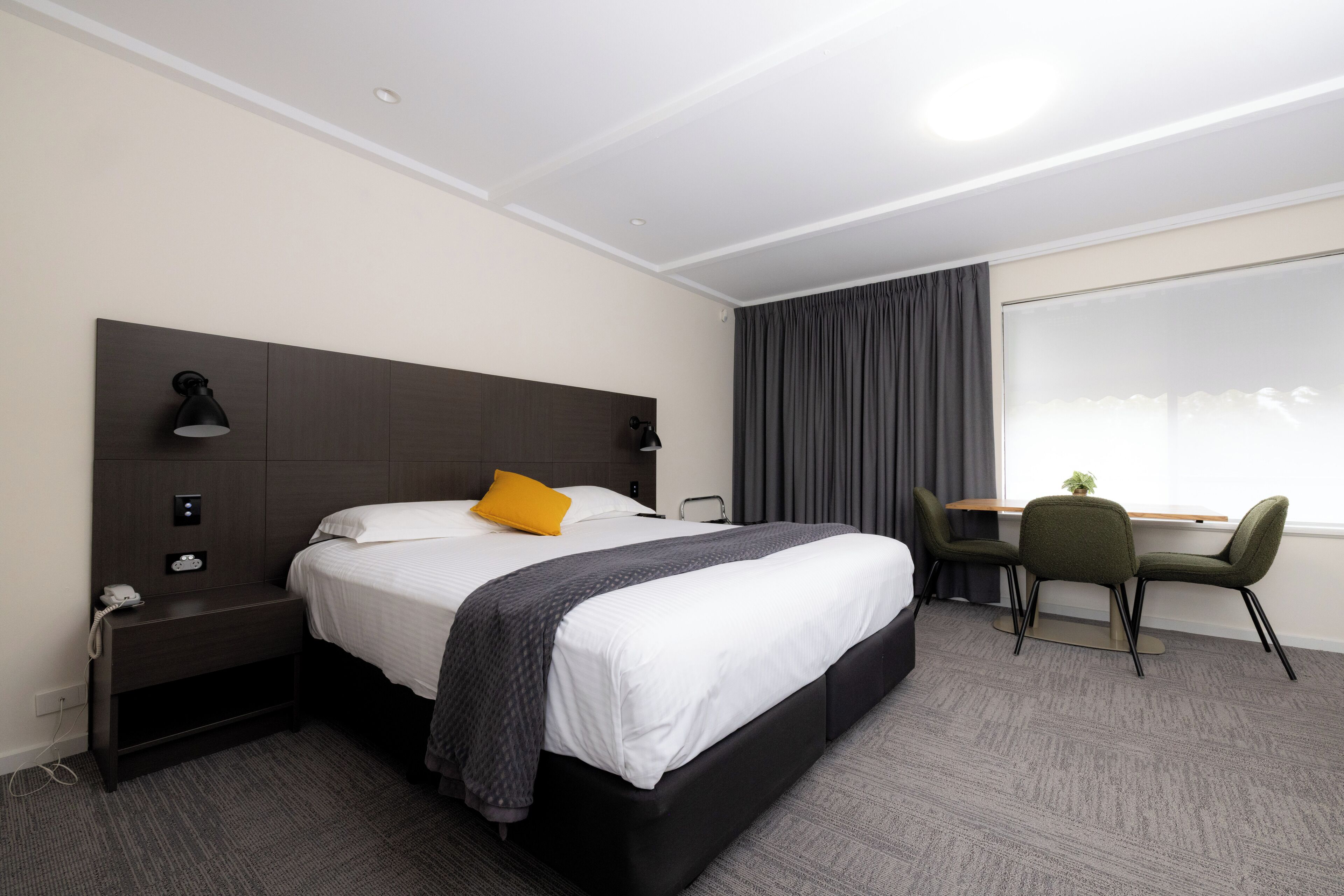 Una habitación de hotel con una cama grande, mesita de noche, lámpara, escritorio y silla.
