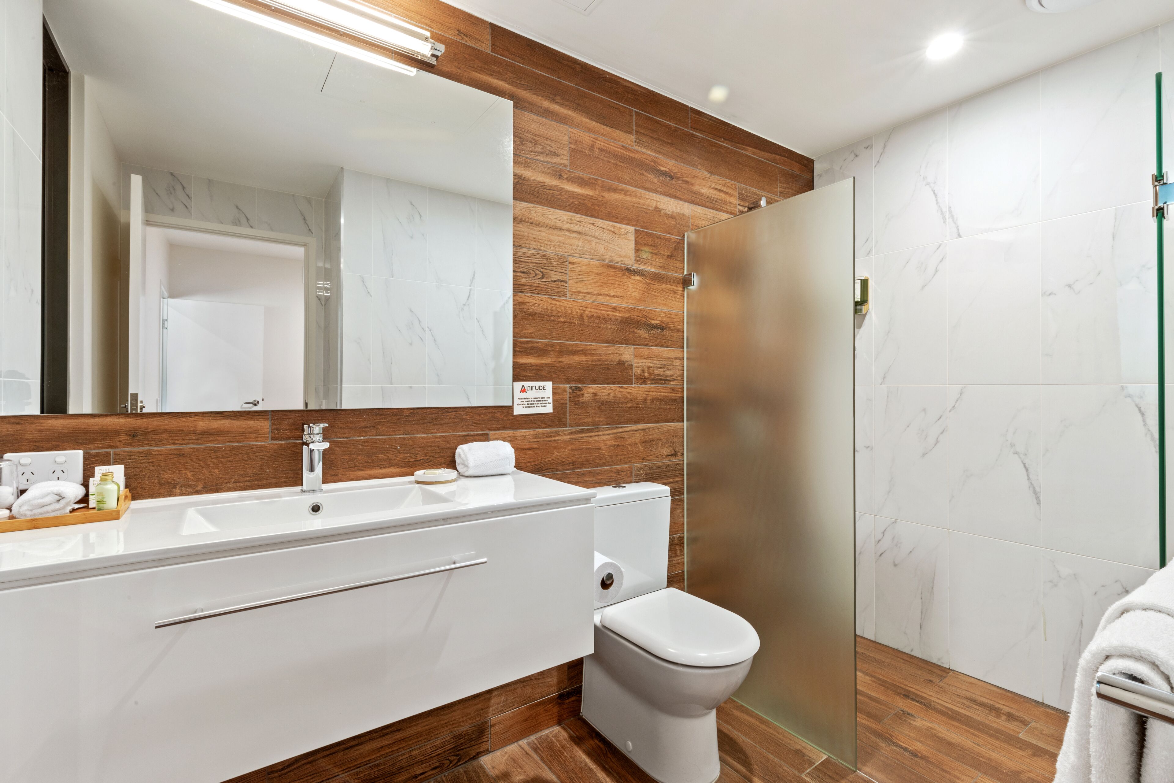Une salle de bain moderne avec un meuble-lavabo en bois, des toilettes blanches et une cabine de douche en verre.