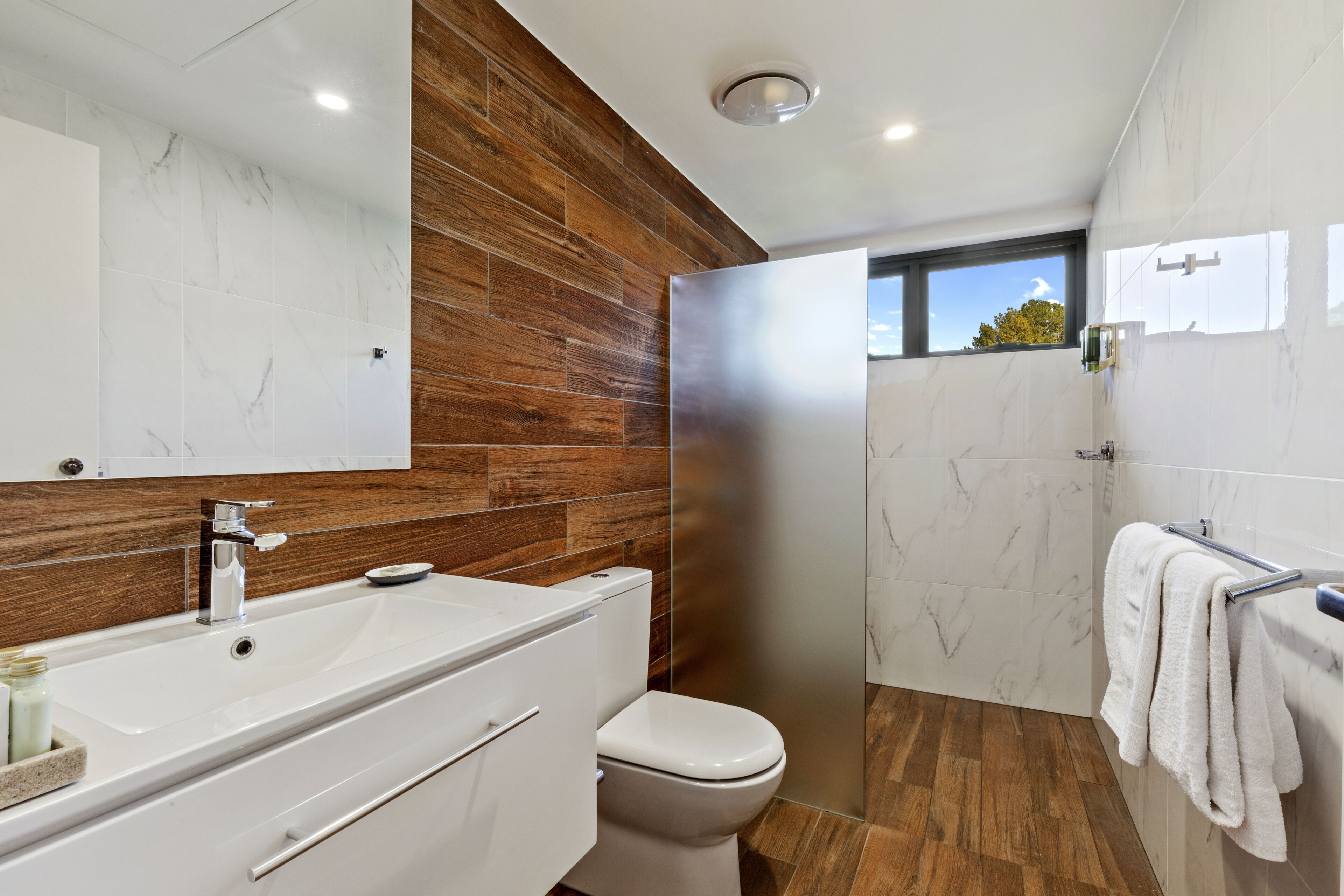 A modern bathroom with a wooden accent wall, a white vanity, a toilet, and a shower area.