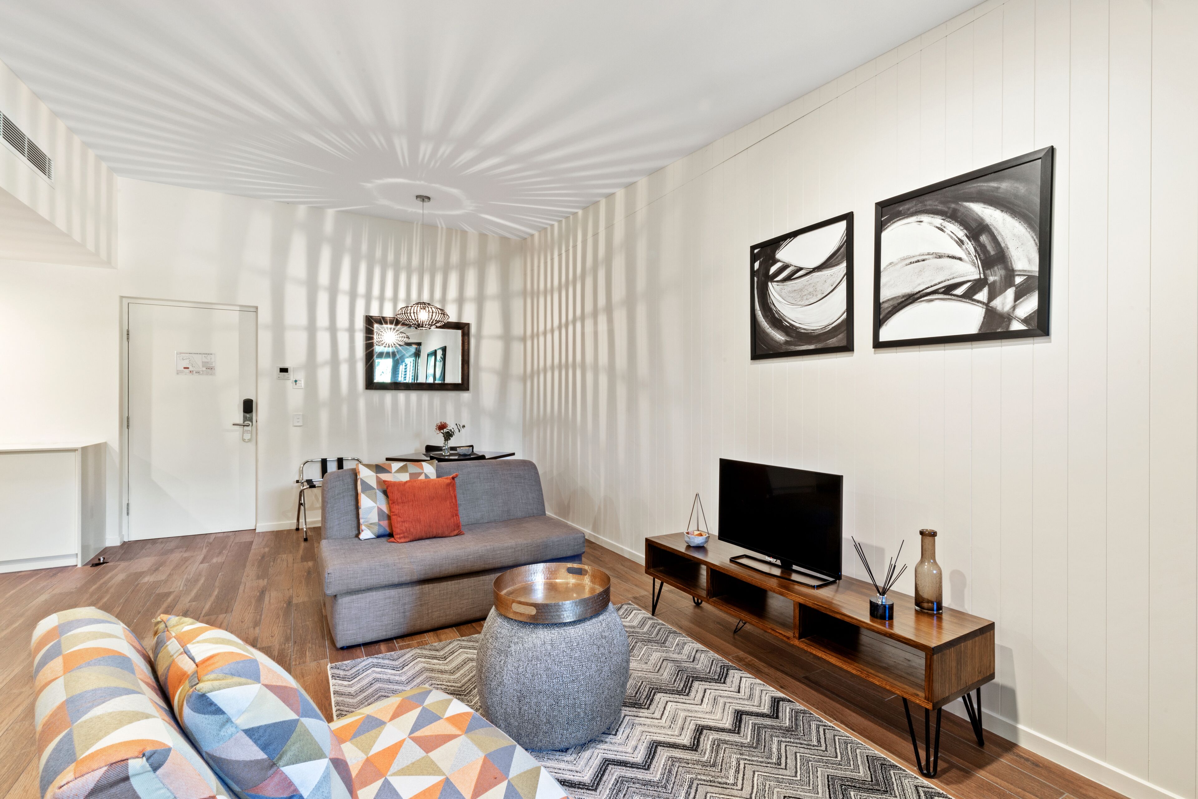 A modern living room with a sofa, ottoman, and a television on a wooden stand.