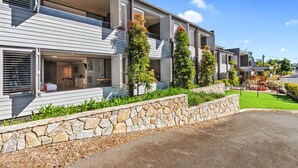 A modern two-story building with a stone retaining wall, balconies, and a landscaped garden.