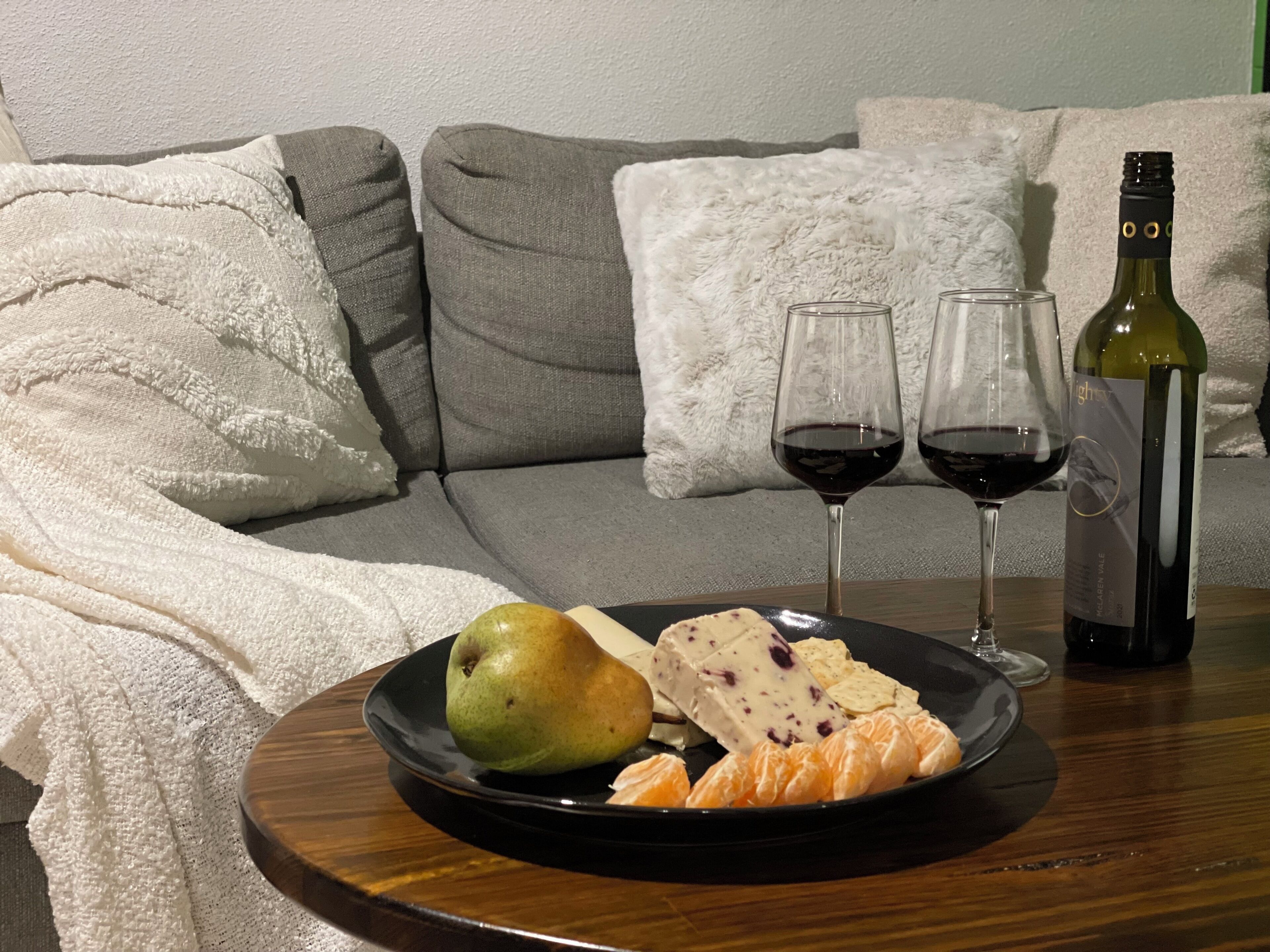 A dining table with a plate of food, two glasses of red wine, and a bottle of wine.