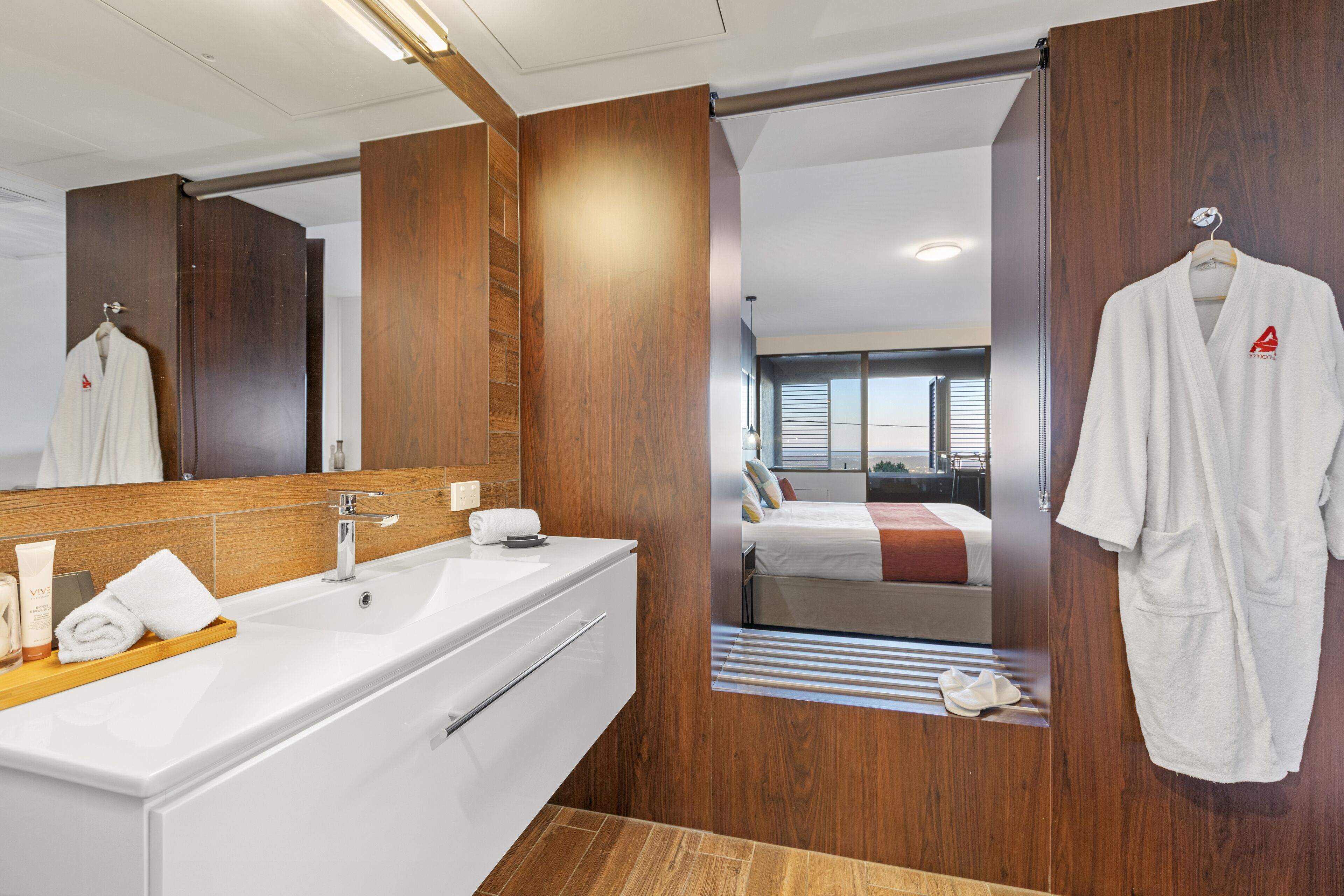 A modern bathroom with a large mirror, wooden paneling, a white sink, and a robe hanging on a rack.