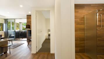 A modern interior with a wooden floor, a glass door leading to a dining area, and a shower with a wooden panel wall.