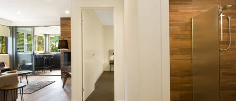 Un interior moderno con piso de madera, una puerta de vidrio que conduce a un comedor y una ducha con pared de paneles de madera.