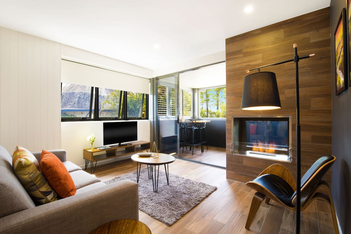 A modern living room with a sofa, TV, fireplace, and a dining area with chairs and a table.