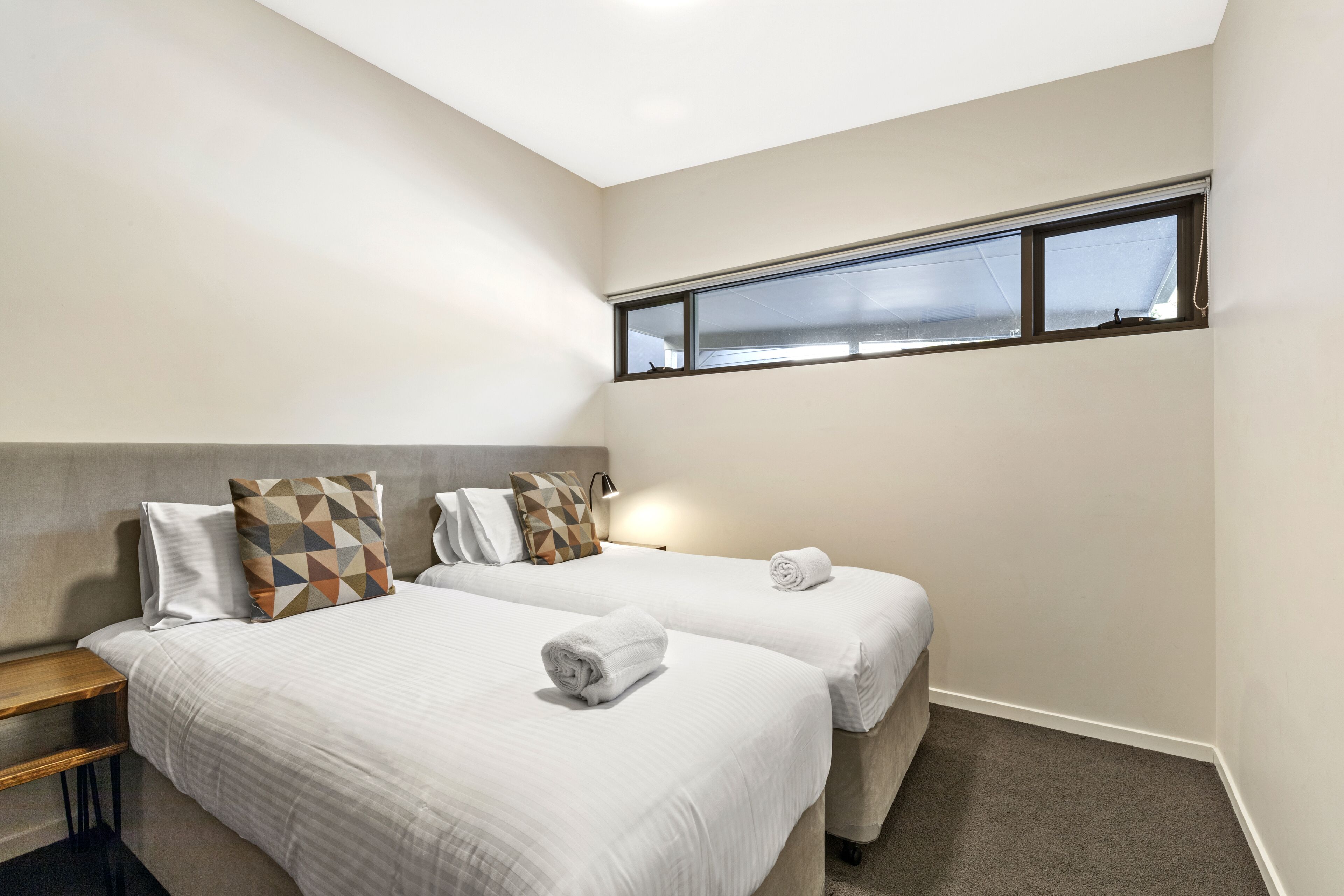 Une chambre d’hôtel avec deux lits, une table de chevet, une fenêtre avec des stores et une lampe.