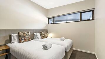 Une chambre d’hôtel avec deux lits, une table de chevet, une fenêtre avec des stores et une lampe.