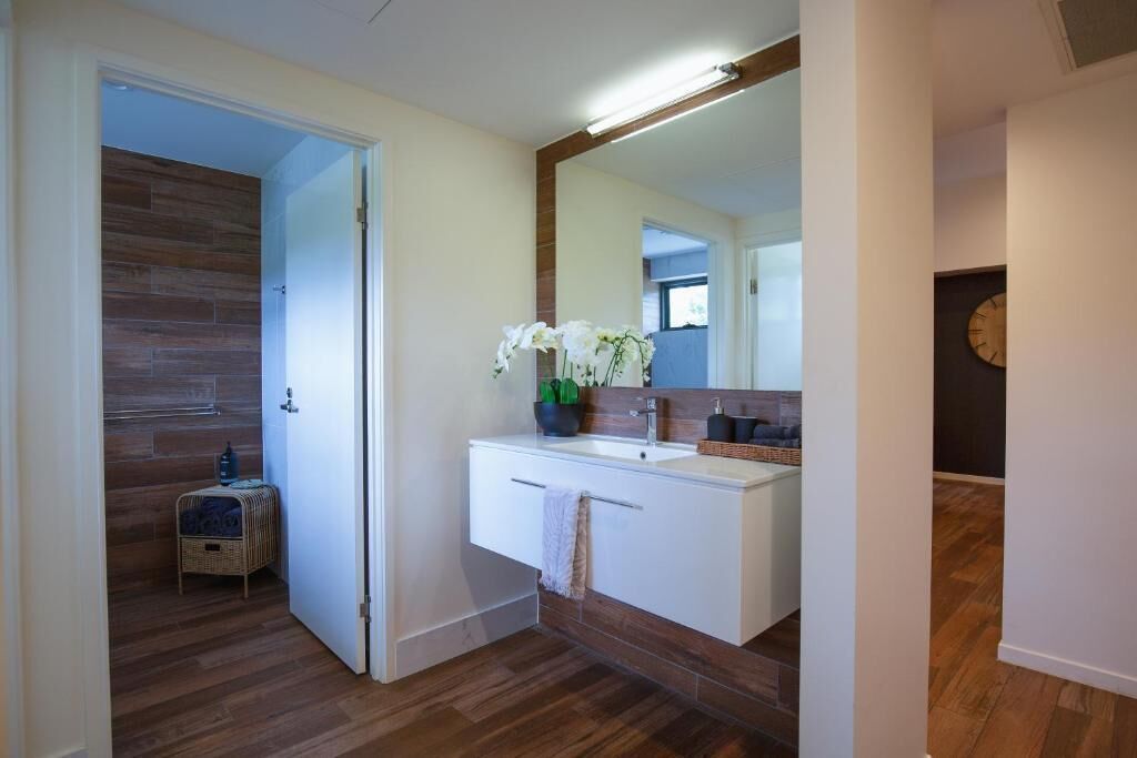 Een badkamer met een houten vloer, een wit wastafeltje met spiegel en een klein rieten mandje.