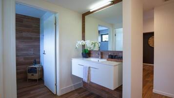 Een badkamer met een houten vloer, een wit wastafeltje met spiegel en een klein rieten mandje.