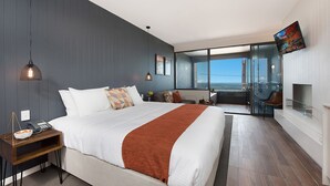 A modern hotel room with a large bed, a desk with a telephone, a small table with a bowl, and a TV mounted on the wall.