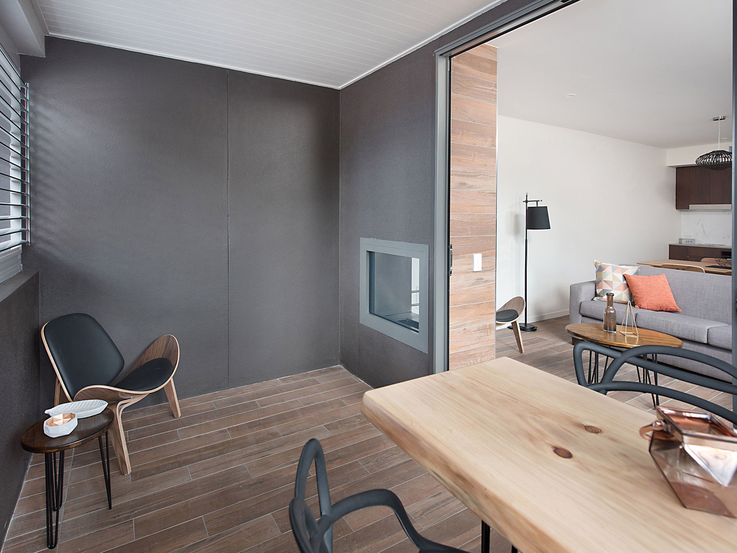 Un interior moderno con una mesa de comedor de madera, dos sillas, un sofá y un televisor montado en la pared.