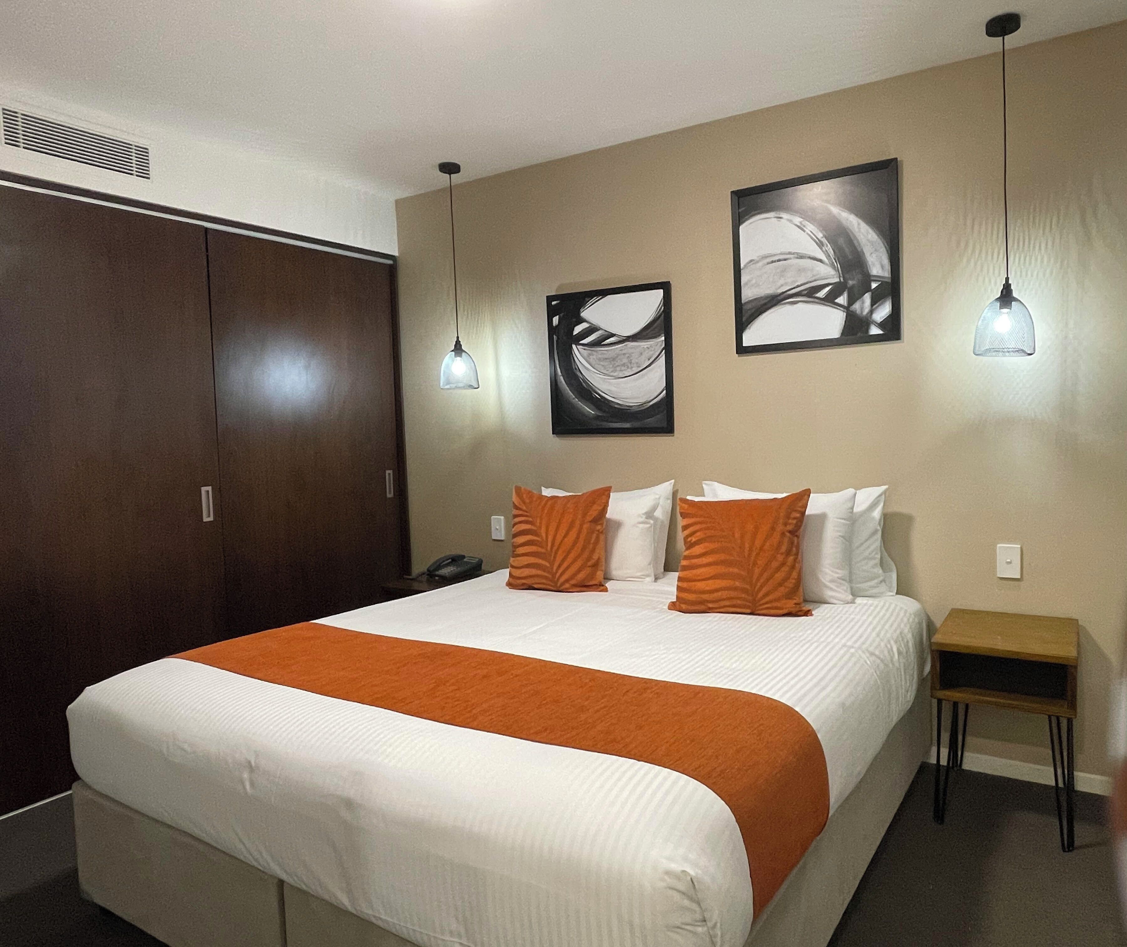 Ett hotellrum med en stor säng, två väggmonterade hänglampor, ett nattduksbord i trä och en garderob.