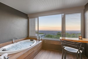 Un baño moderno con una bañera grande, suelo de madera y vistas amplias por las ventanas.