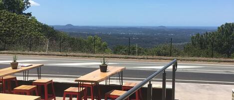 An outdoor seating area with tables and chairs, a railing, and a view of a road and distant landscape.