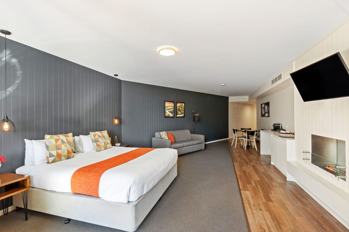 A modern hotel room with a large bed, a sofa, a dining area, and a TV mounted on the wall.
