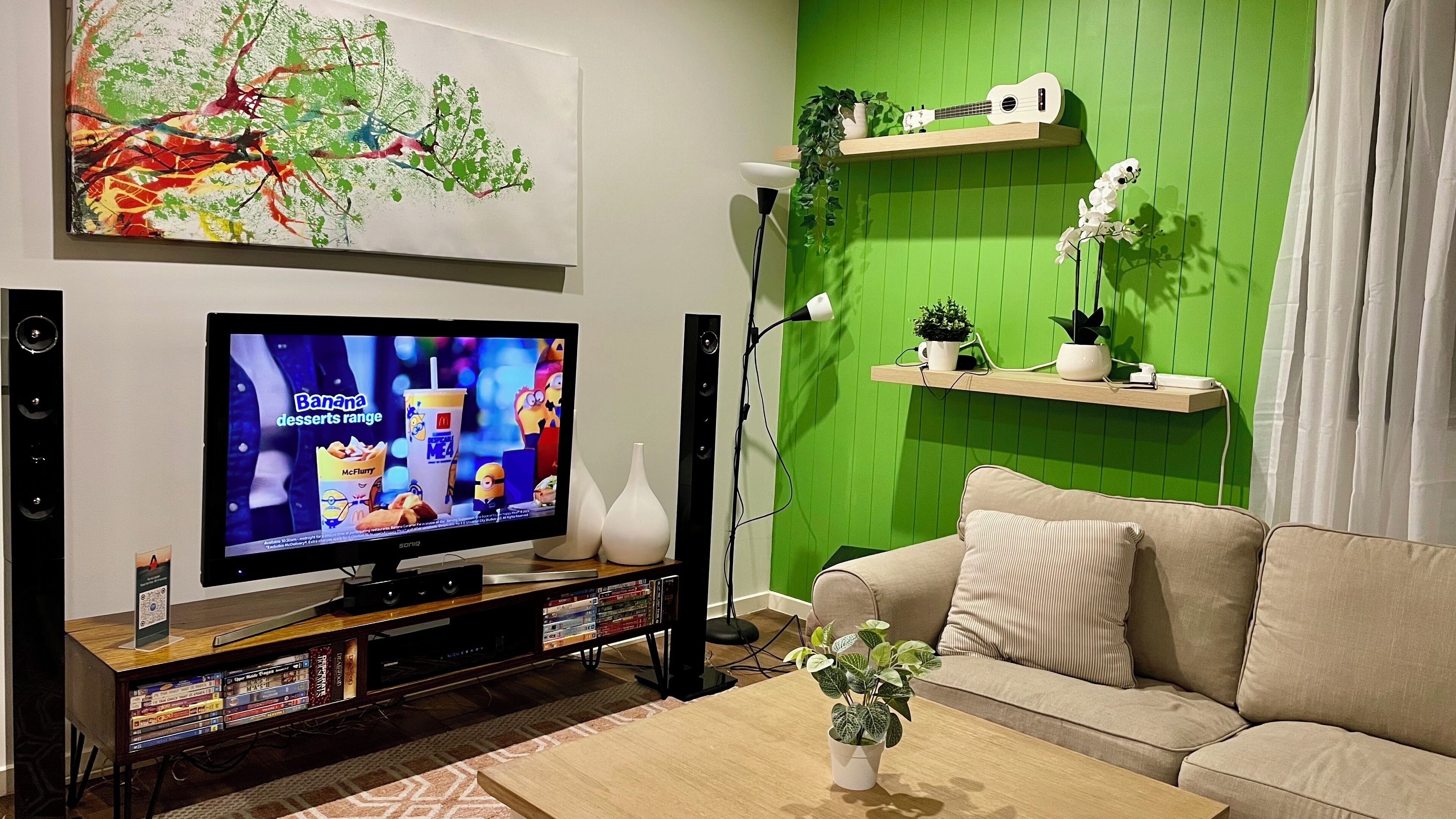 Una sala de estar con televisor de pantalla plana, estantería, pared de acento verde, sofá y mesa de centro.