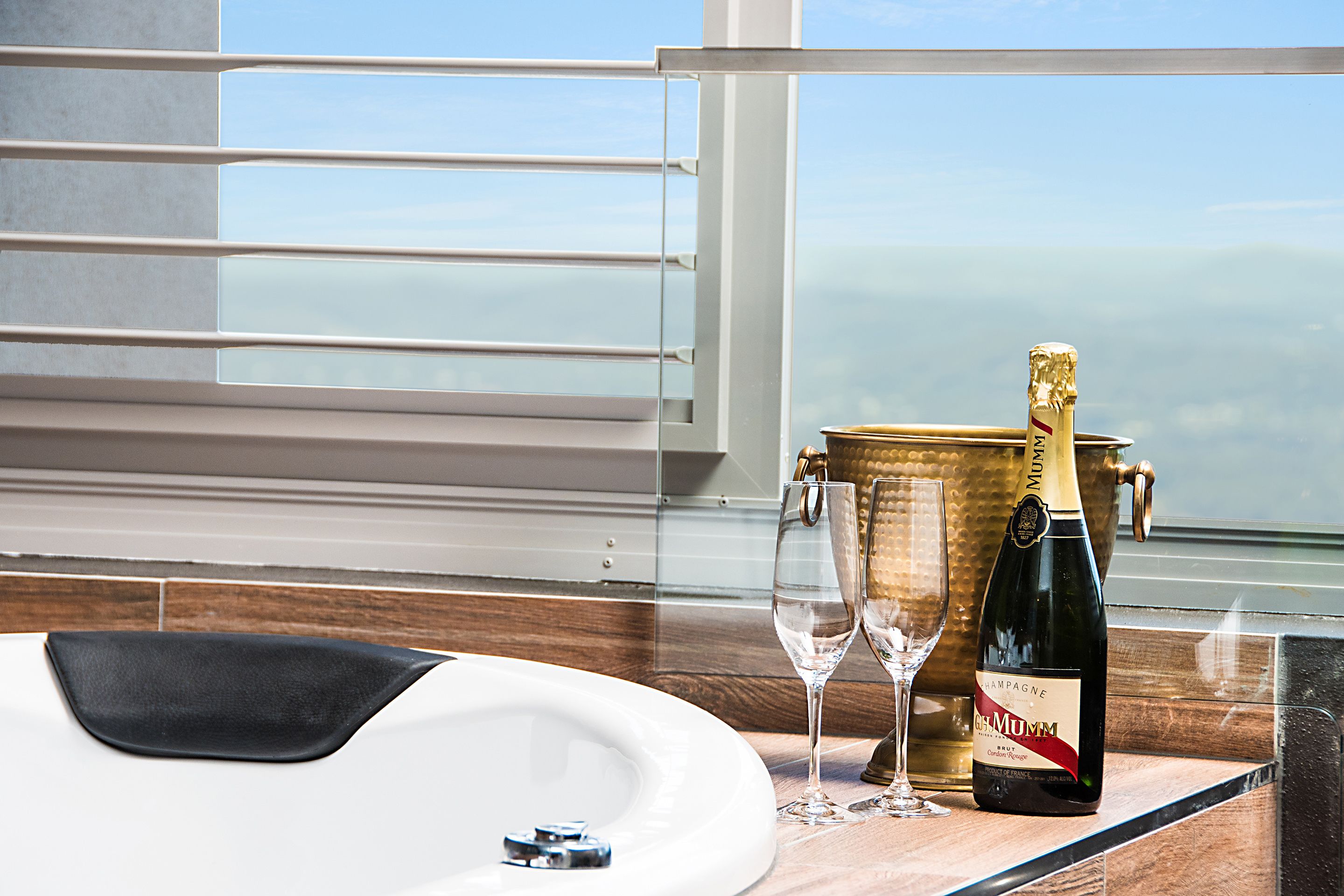 Une bouteille de champagne et des verres sur un comptoir en bois, avec vue sur l’océan par la fenêtre.