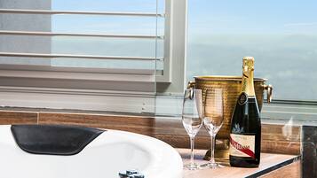 Une bouteille de champagne et des verres sur un comptoir en bois, avec vue sur l’océan par la fenêtre.