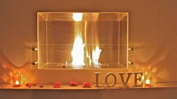 Una chimenea con frente de vidrio transparente, la palabra 'LOVE' debajo y flores rosadas en la base.