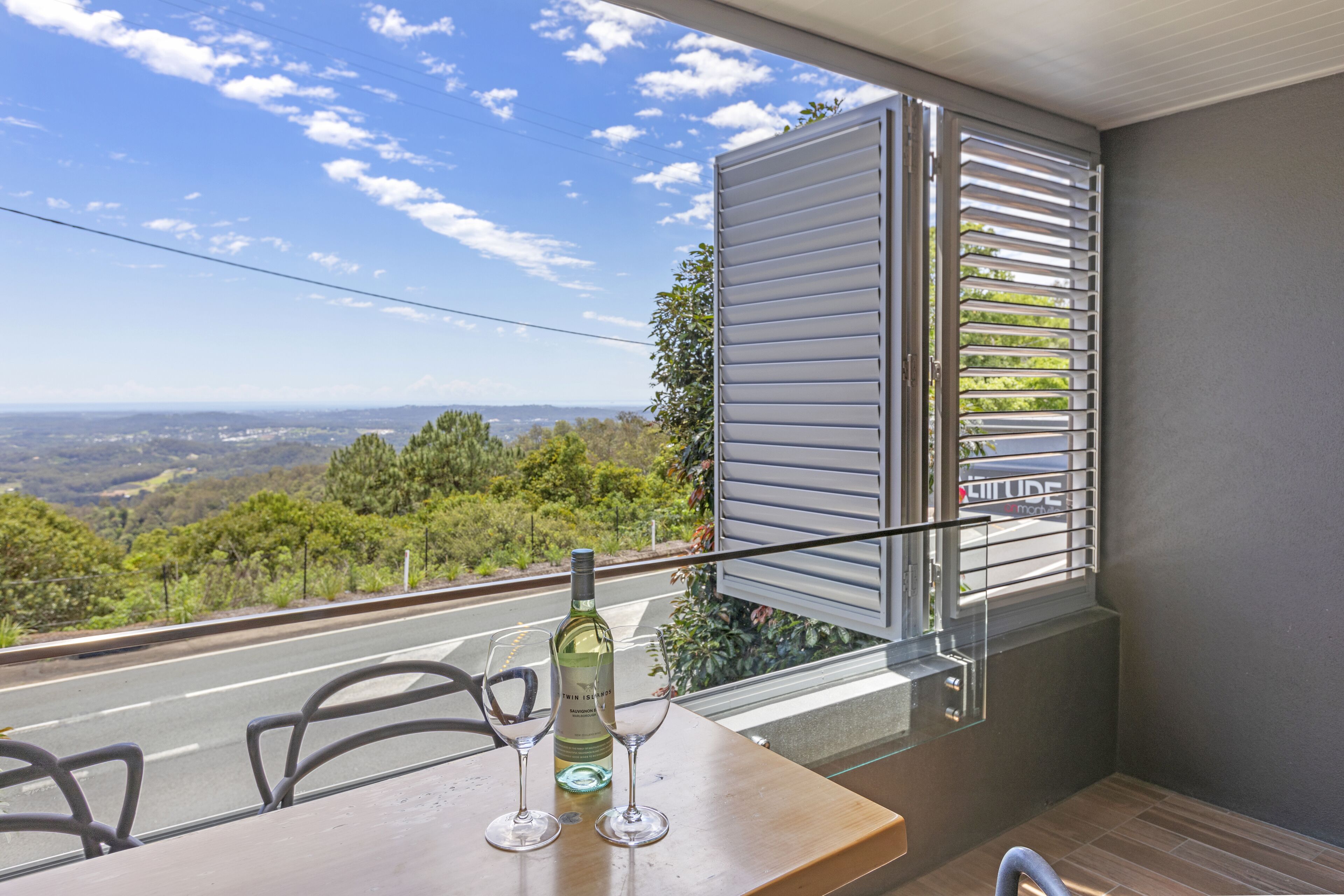 Un balcon avec une table, deux verres à vin et une bouteille de vin.