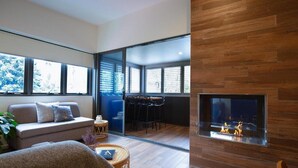 A modern living room with a fireplace, a sofa, a dining area, and large windows.