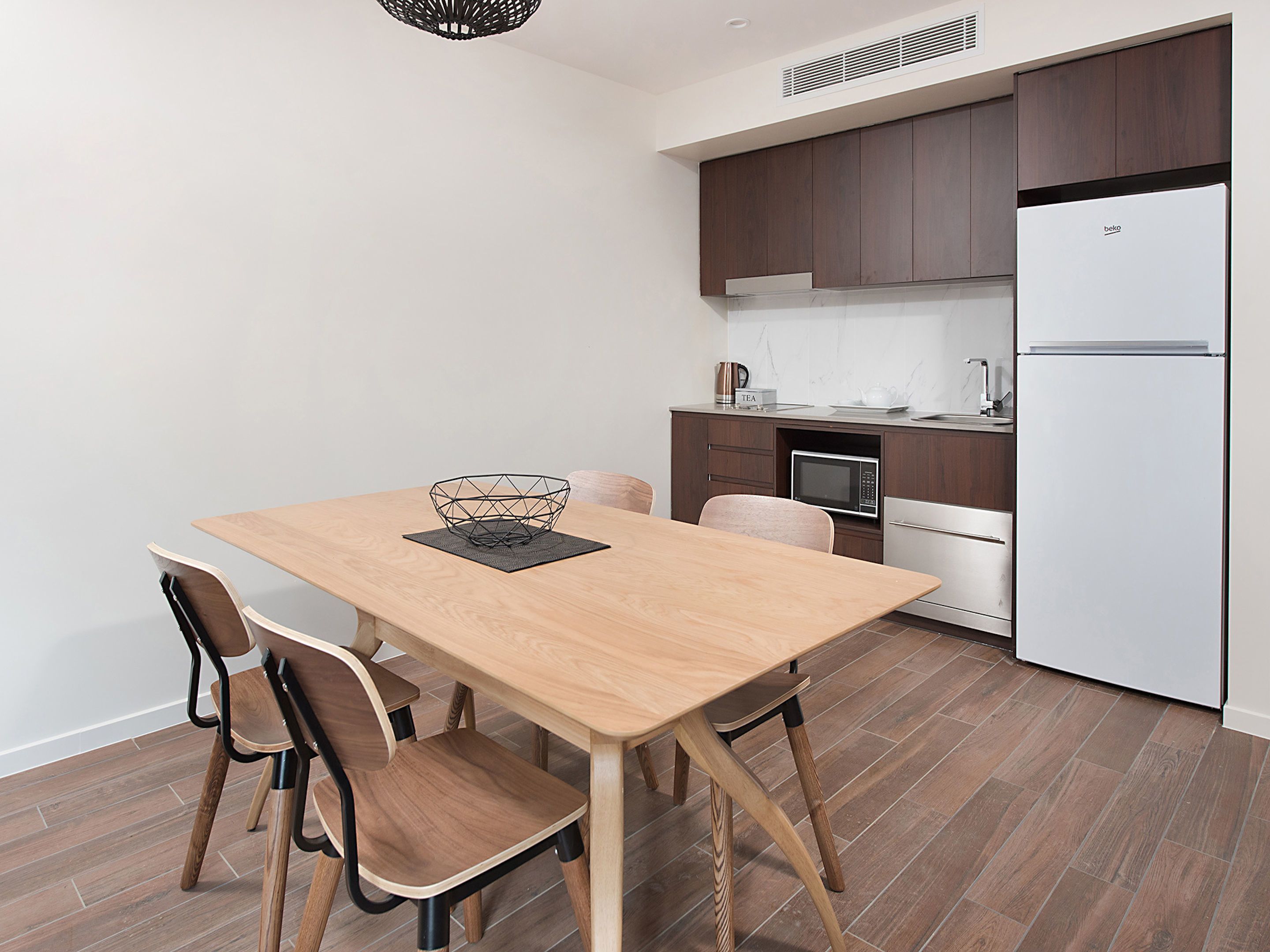 A modern kitchen with a wooden table, chairs, a microwave, and a white refrigerator.