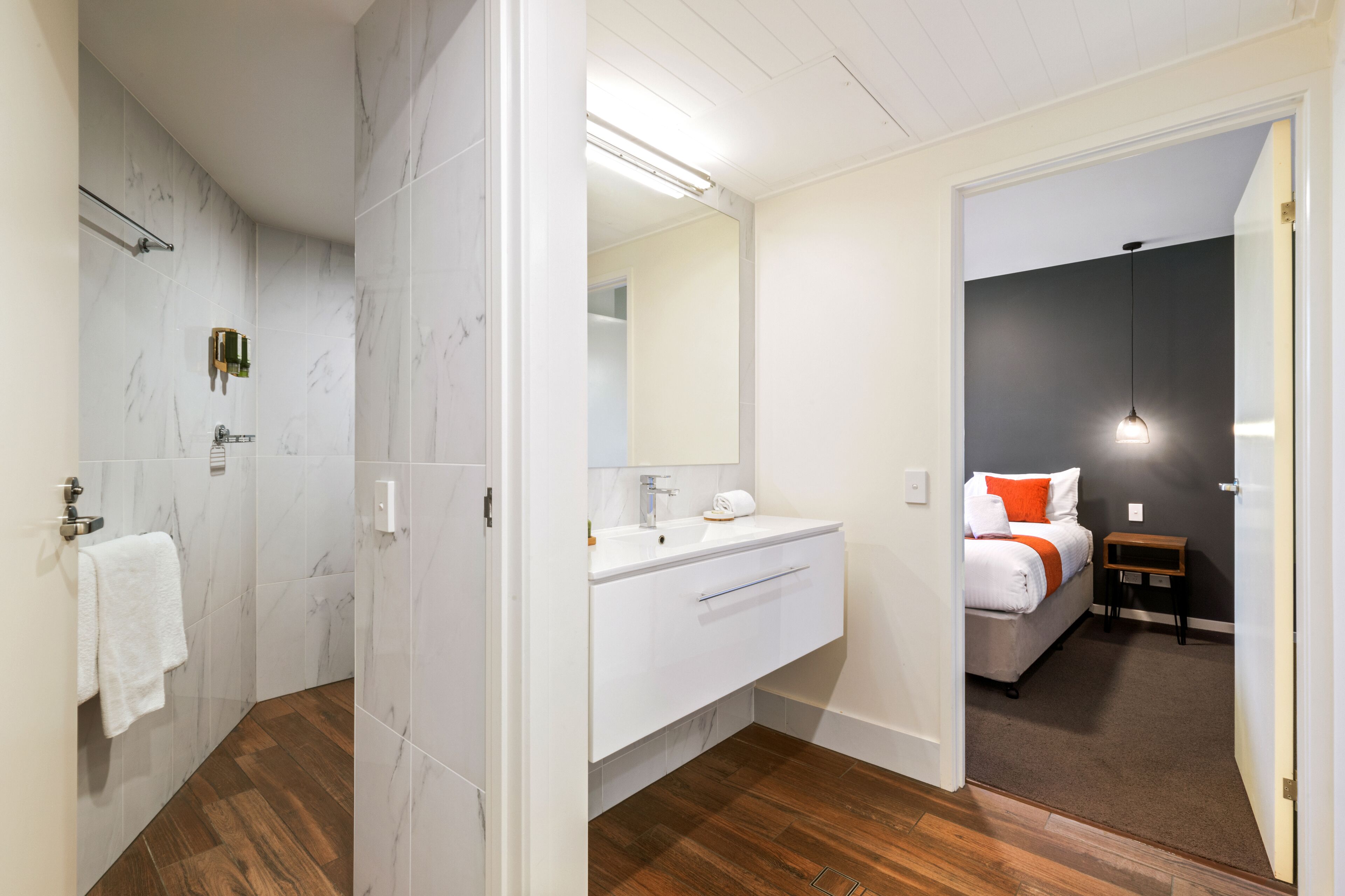 Een badkamer met een douche, een wastafel en een spiegel. Een handdoek hangt aan een rek.