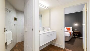 Een badkamer met een douche, een wastafel en een spiegel. Een handdoek hangt aan een rek.